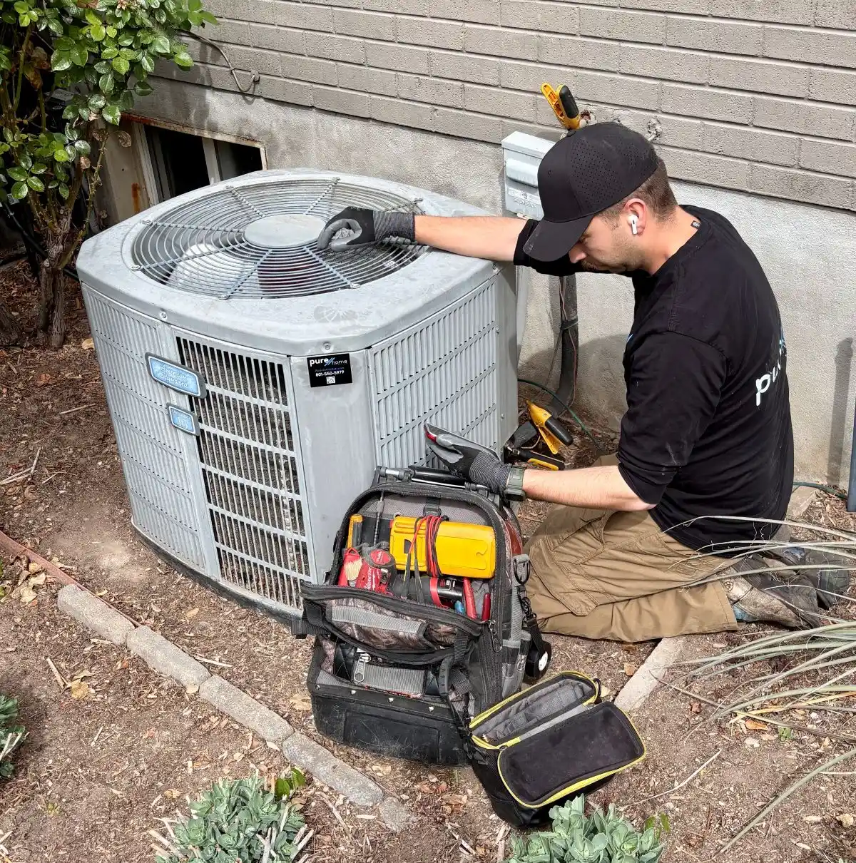 purehome-hvac-maintenance-tune-up-riverton-ut PureHome Heating & Air technician performing an HVAC maintenance tune-up and inspecting an outdoor air conditioning unit in Riverton, Utah.